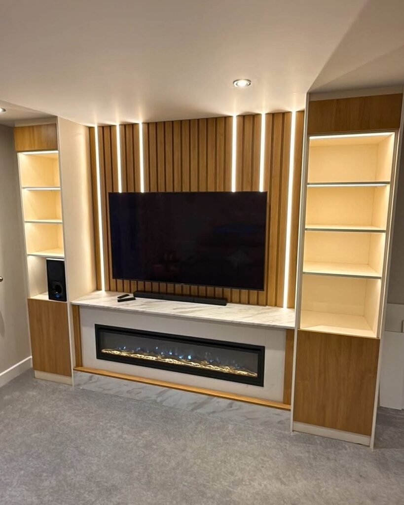 Small lounge cabinet setup featuring a wall-mounted TV on vertical wood slats with LED lighting, flanked by illuminated shelving and a sleek electric fireplace  ideal for compact, modern living rooms.